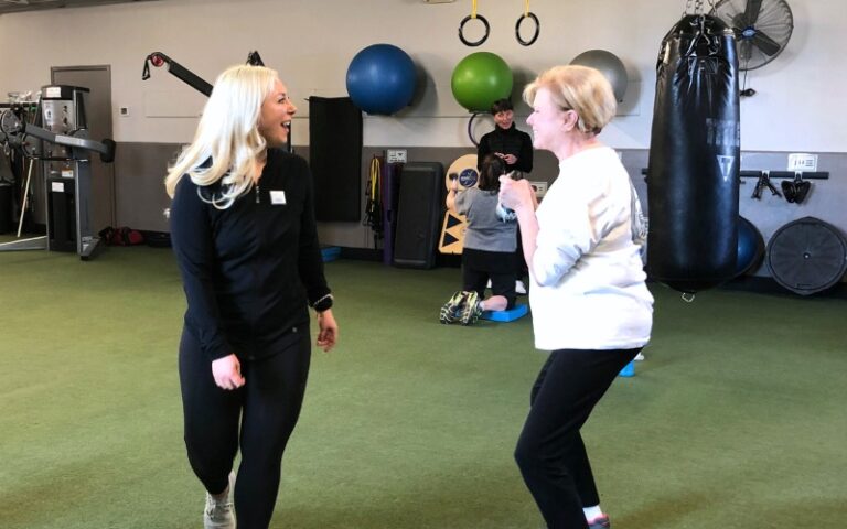 a certified personal trainer spots a gym member during a kettle bell squat in a functional turf training area at a furlong gym