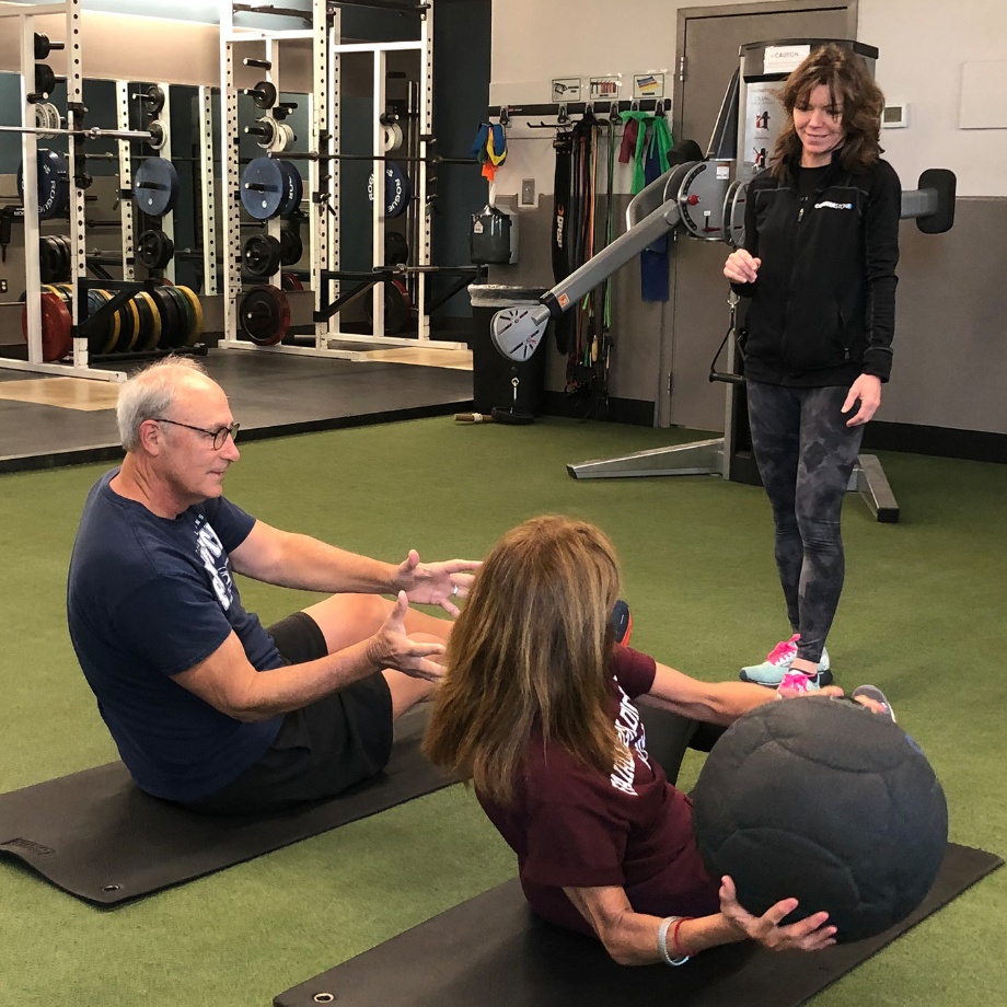 2 gym members pass a weighted ball while holding a seated core position during a personal training session at a doylestown cornerstone health & fitness