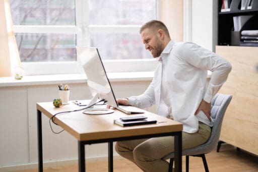 Man sitting at his desk rubbing his aching back