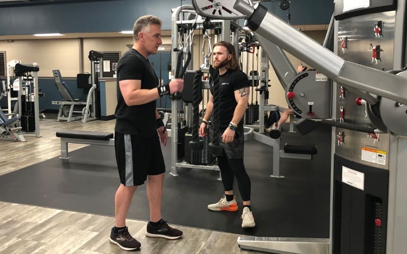 a personal trainer at a bucks county gym helps a gym member with a cable workout