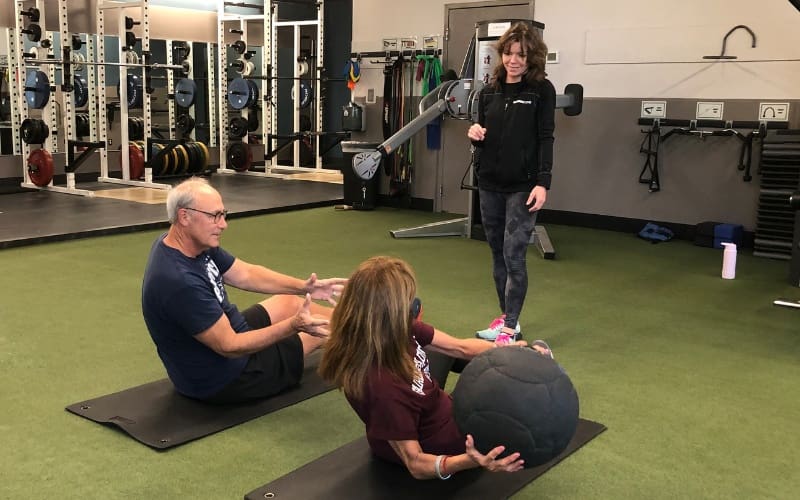 two gym members pass a weighted ball with a certified personal trainer during a core workout in a functional training zone at a buck's county gym
