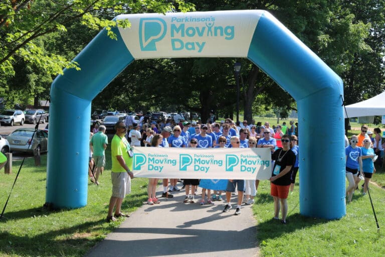 A crowd of people crossing the finish line of the Moving Day Walk for theParkinson's Foundation.