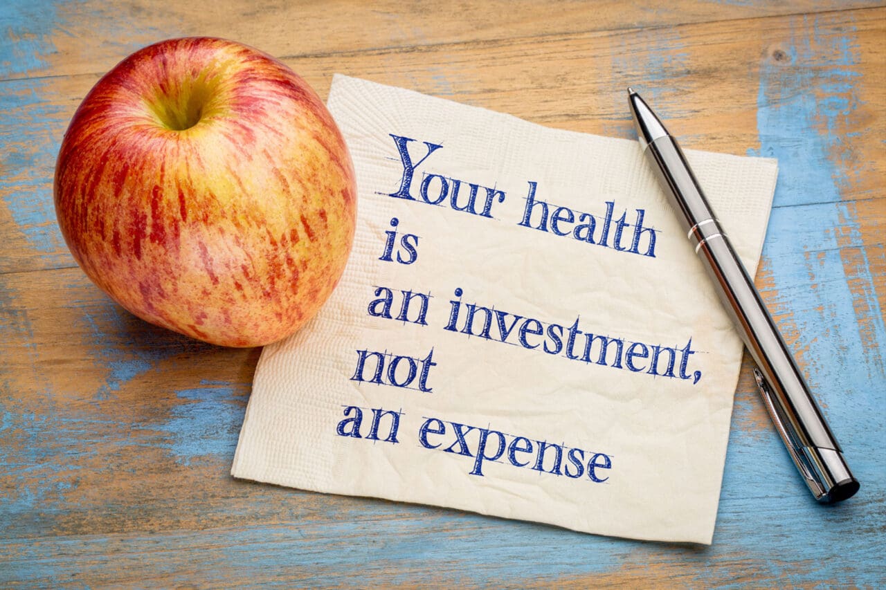 Photo of an apple and a note which states Your Health is an Investment, not an expense.