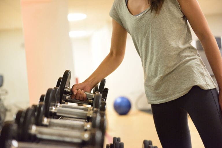 Woman lifting a dumbbell off a weight rack.