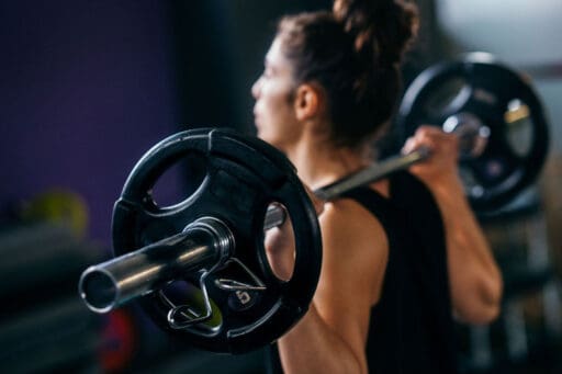 Woman lifting a barbell on her back.