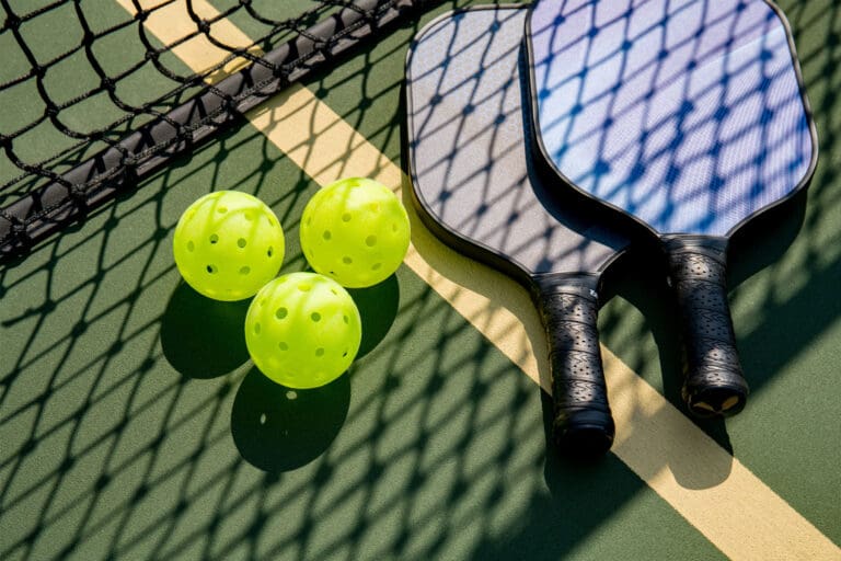 Pickleball paddles and a ball laying on a pickleball court.