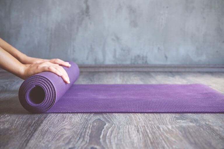 Person unrolling a yoga mat on the floor.